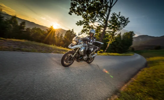 Motorradfahrer auf kurviger Straße bei Sonnenuntergang in ländlicher Umgebung