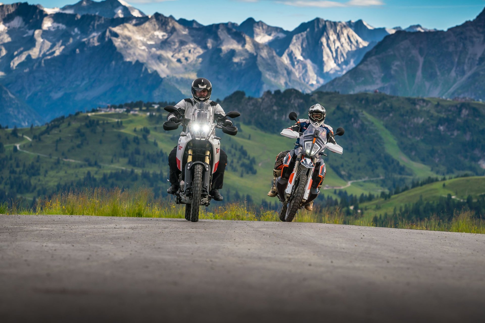 Zwei Motorradfahrer fahren auf Bergstraße mit Alpen im Hintergrund