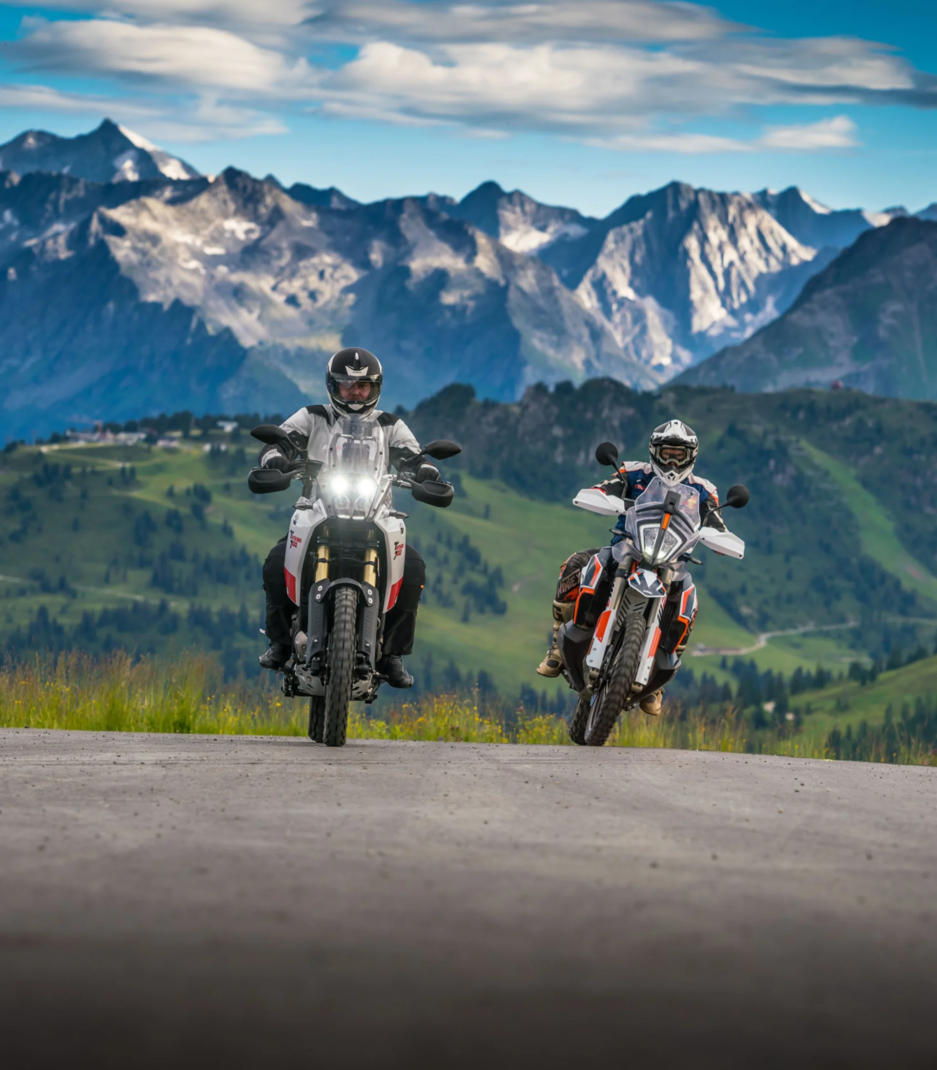 Two motorcyclists riding on mountain road with Alps in background
