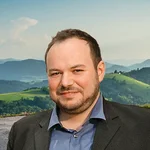 Mann in Sakko vor grünen Hügeln und bewölktem Himmel