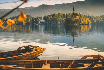 Bled & Soriška Planina Adventure Boote auf See mit Insel und Kirche im Hintergrund im Herbst