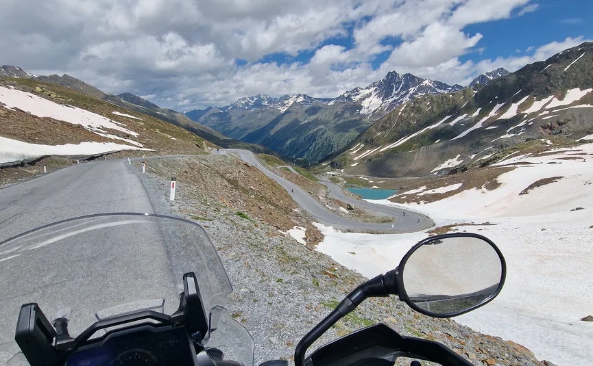 View from motorcycle on winding mountain road with snow and mountains