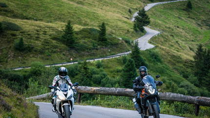 Zwei Motorradfahrer auf kurviger Bergstraße mit grünem Wald im Hintergrund