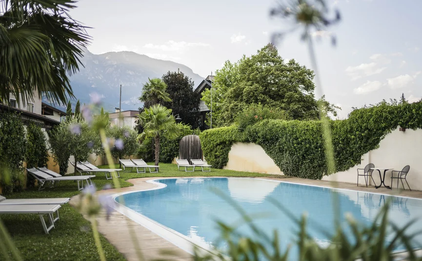 Outdoor pool with lounge chairs and table near hedge and mountains