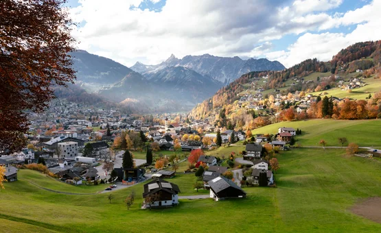 Bergdorf mit Häusern und grünen Wiesen im Herbst vor bewölkten Alpen