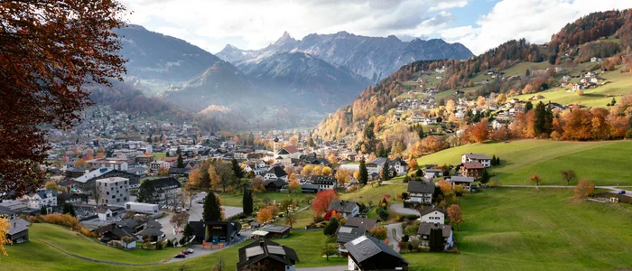 Mountain village with houses and green fields in autumn under cloudy Alps