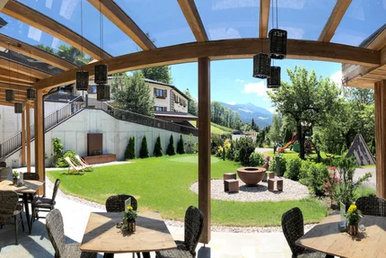 Überdachte Terrasse mit Tischen, Stühlen und Bergblick in einem Garten