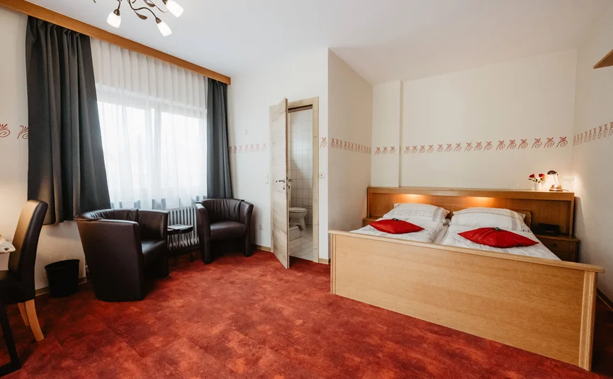 Cozy hotel room with double bed, armchairs, and open bathroom door