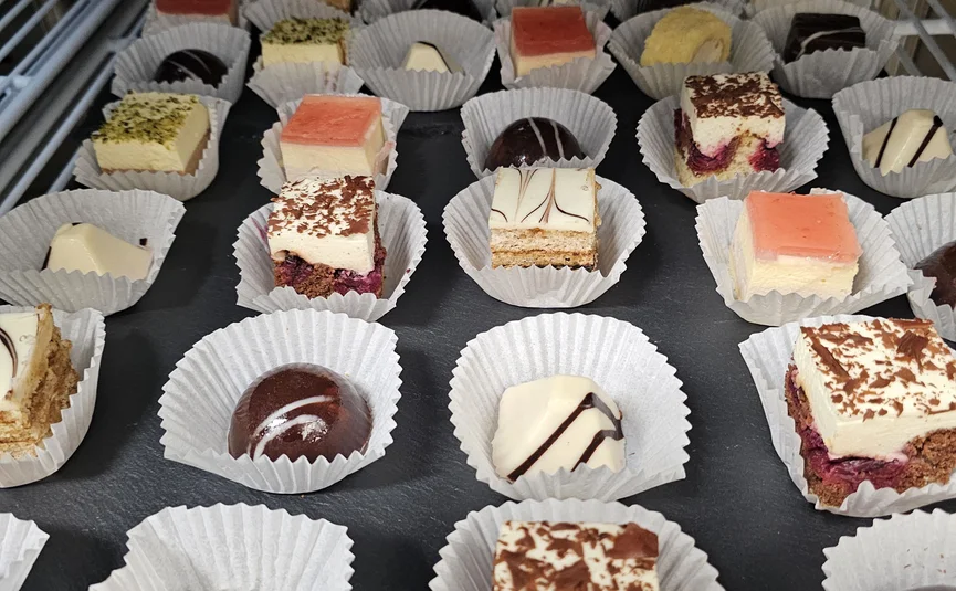 Assorted small chocolates and cake pieces in paper cups on tray