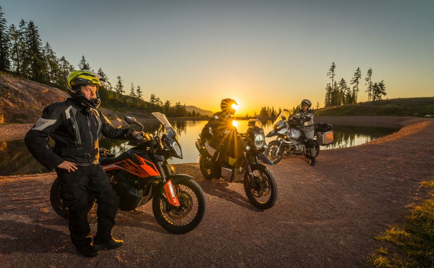 Motorradfahrer mit Helmen an einem See bei Sonnenuntergang