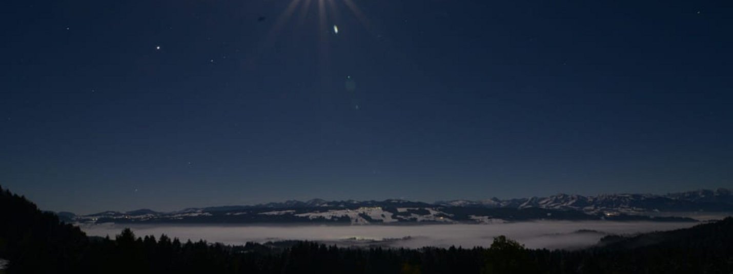 Mondschein über schneebedeckter Landschaft mit Bergen im Hintergrund