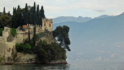 Alte Burg am Seeufer mit Zypressen und Bergblick im Hintergrund