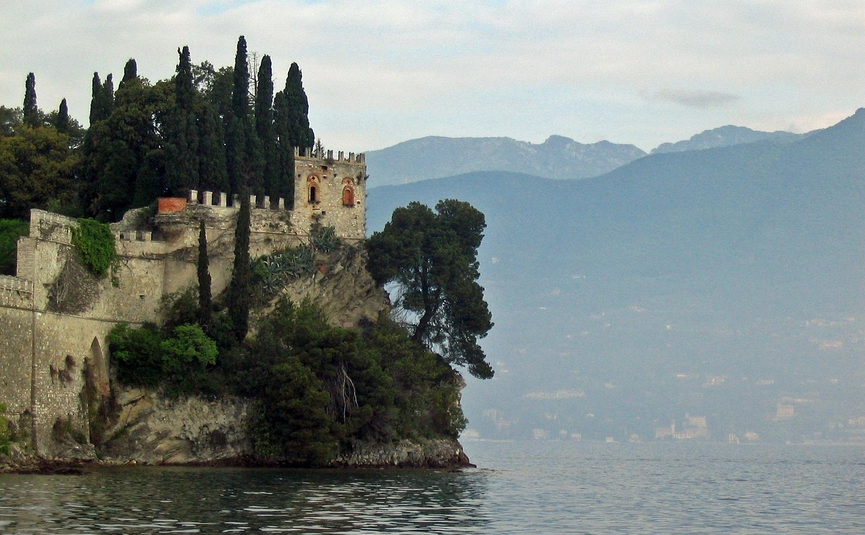 Alte Burg am Seeufer mit Zypressen und Bergblick im Hintergrund
