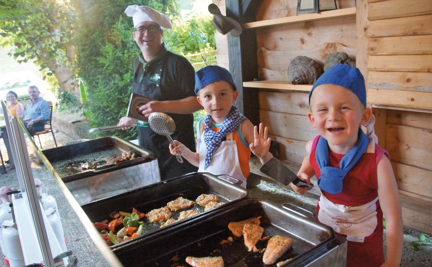 Zwei Kinder und ein Mann kochen zusammen draußen auf einem Grill