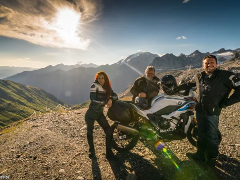 Drei Personen mit BMW-Motorrad auf Bergstraße bei Sonnenschein