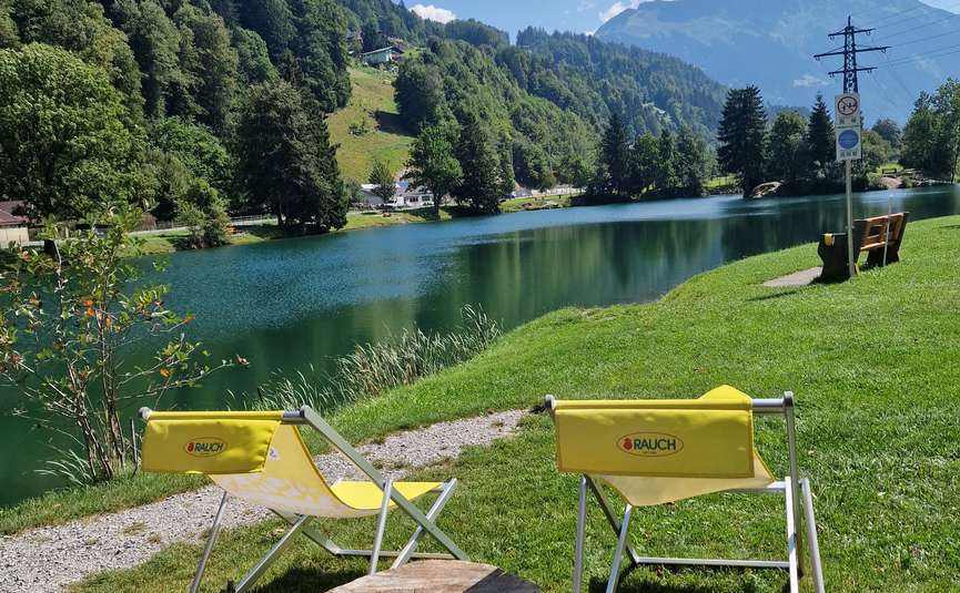 MoHo Schönauer Hof Tour 10 "Lake Tour-Kühtai" Two yellow chairs by a lake with mountain view under blue sky