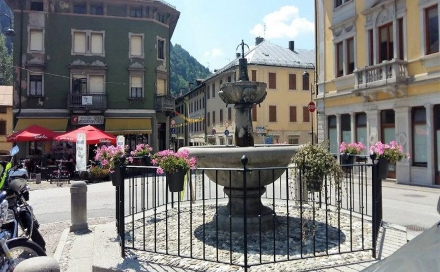 Steinerner Brunnen mit Blumen und umliegenden historischen Gebäuden