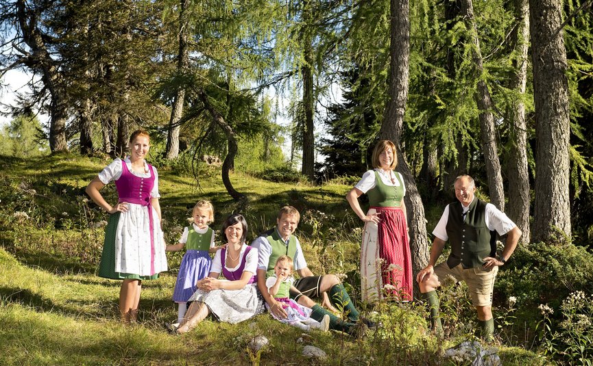 Almhotel & Genussgasthof Hierzegger ***S © Rupert Mühlbacher GAService Familie in traditioneller Tracht sitzt und steht im Wald an einem sonnigen Tag