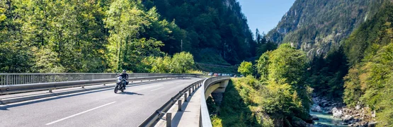 Motorradfahrer auf Brücke über Fluss in gebirgiger Waldlandschaft