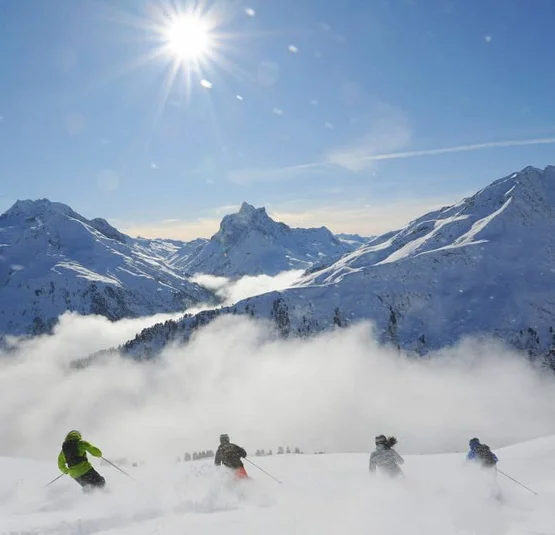 Skifahrer fahren durch Tiefschnee vor verschneiten Bergen in der Sonne