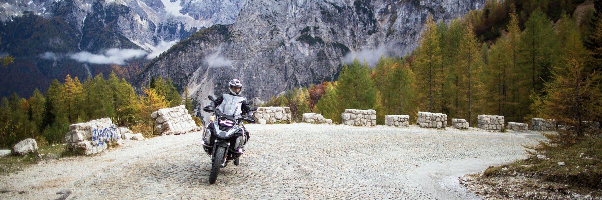 Motorradfahrer auf steiniger Bergstraße mit hohen Felsen und Bäumen
