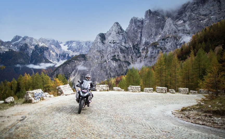 Motorradfahrer auf steiniger Bergstraße mit hohen Felsen und Bäumen