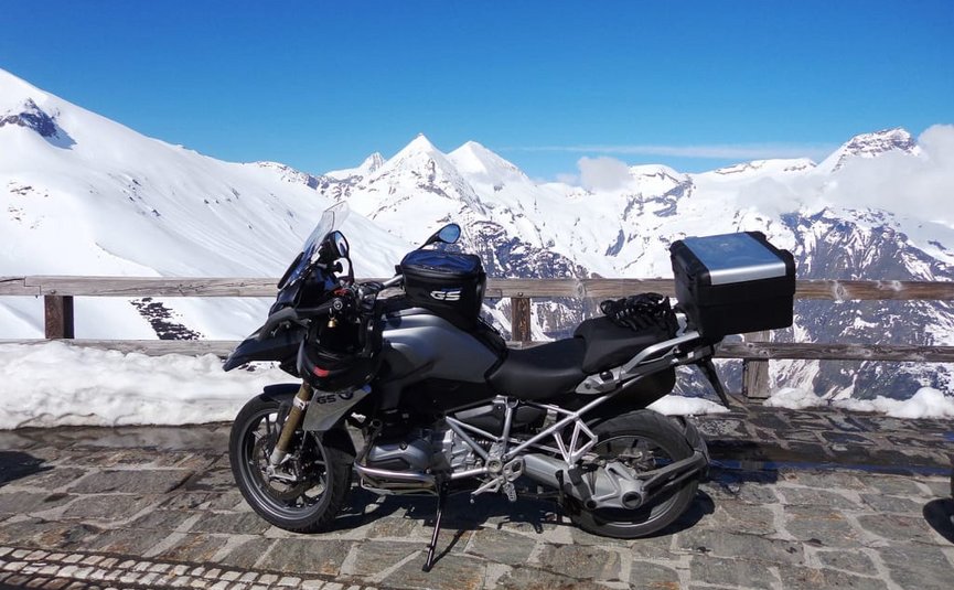 Motorrad auf steinigem Aussichtspunkt mit schneebedeckten Bergen im Hintergrund