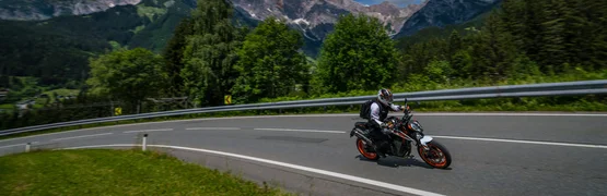 Motorvakantie in SalzburgerLand Motorrijder op kronkelende bergweg met beboste bergen op de achtergrond