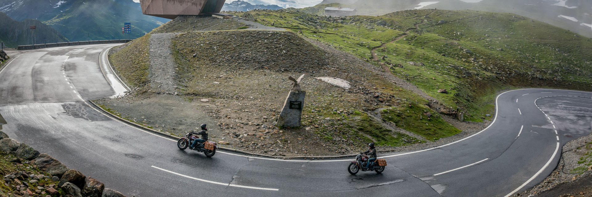Kurvenreiche Bergstraße mit zwei Motorradfahrern und Aussichtspunkt im Nebel
