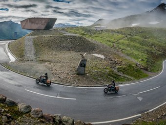 Kurvenreiche Bergstraße mit zwei Motorradfahrern und Aussichtspunkt im Nebel