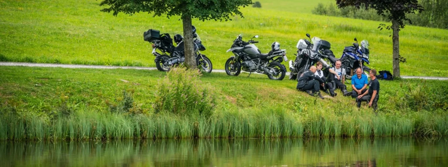 MOTORRAD - Genuss-Tage So-Do 2026/27 Vijf mensen zitten bij een meer met motoren op een groene wei