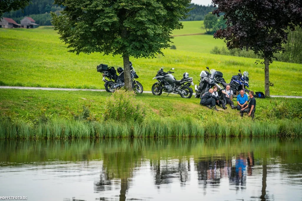 MOTORRAD - Genuss-Tage So-Do 2026/27 Vijf mensen zitten bij een meer met motoren op een groene wei