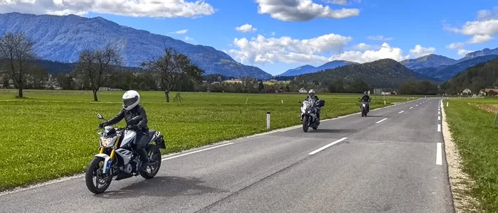 Three motorcyclists riding on a country road with mountains in the background