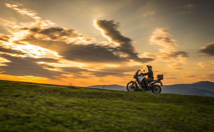 Motorradfahrer auf grünem Hügel bei Sonnenuntergang mit dramatischem Himmel