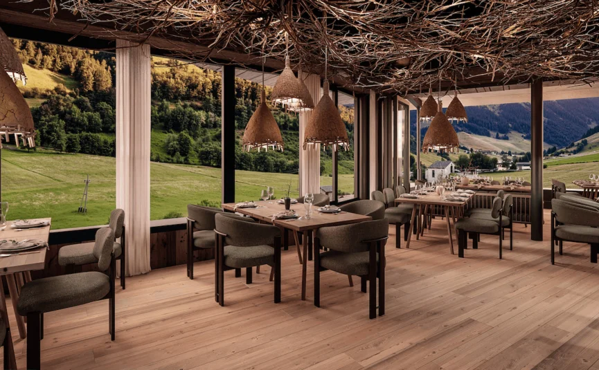 Restaurant mit Holztischen, Zweig­decke und Panoramablick auf grüne Berglandschaft