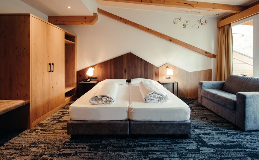 Gemütliches Hotelzimmer mit zwei Betten, Sofa und Holzmöbeln unter Dachschräge