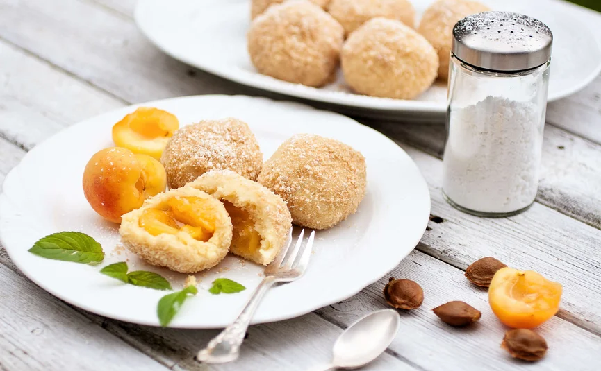 Apricot dumplings with sugar on white plate and sugar shaker on wooden table