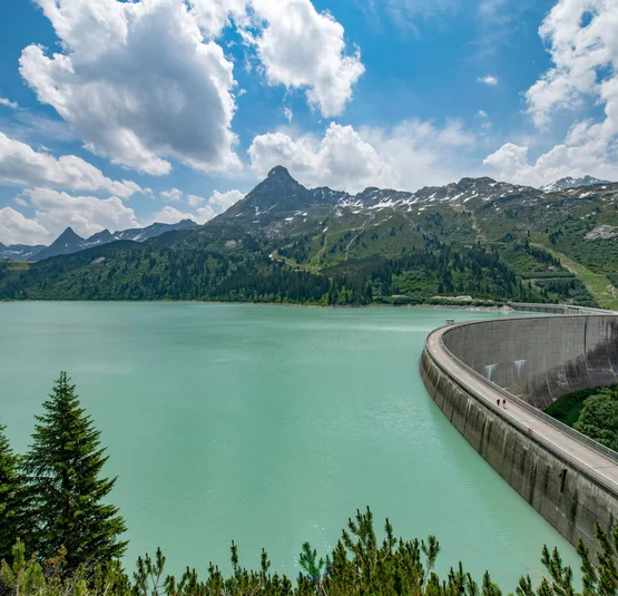 Stausee mit Bergkulisse und Staumauer unter blauem Himmel mit Wolken