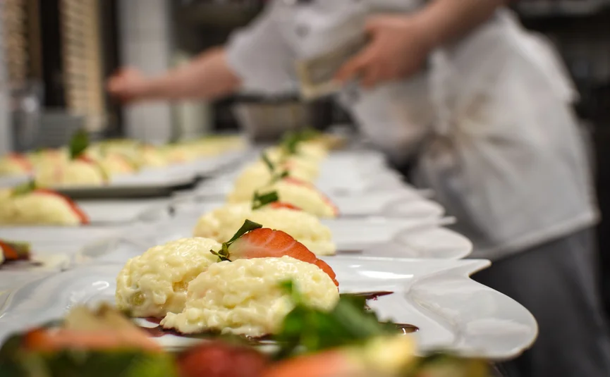 Row of dessert plates with cream, strawberries and mint, kitchen staff in the background
