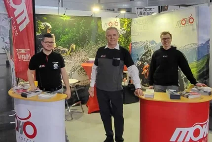 Drie mannen bij beursstand met motorinformatie en brochures