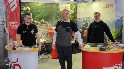 Drei Männer an Messestand mit Motorradinformationen und Broschüren