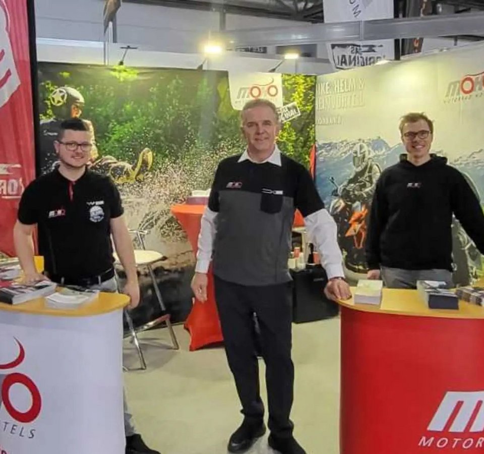 Drei Männer an Messestand mit Motorradinformationen und Broschüren