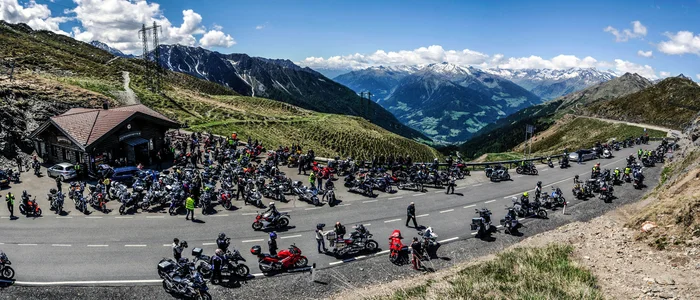 Motorradfahrer versammeln sich an einem Bergpass mit Alpenpanorama