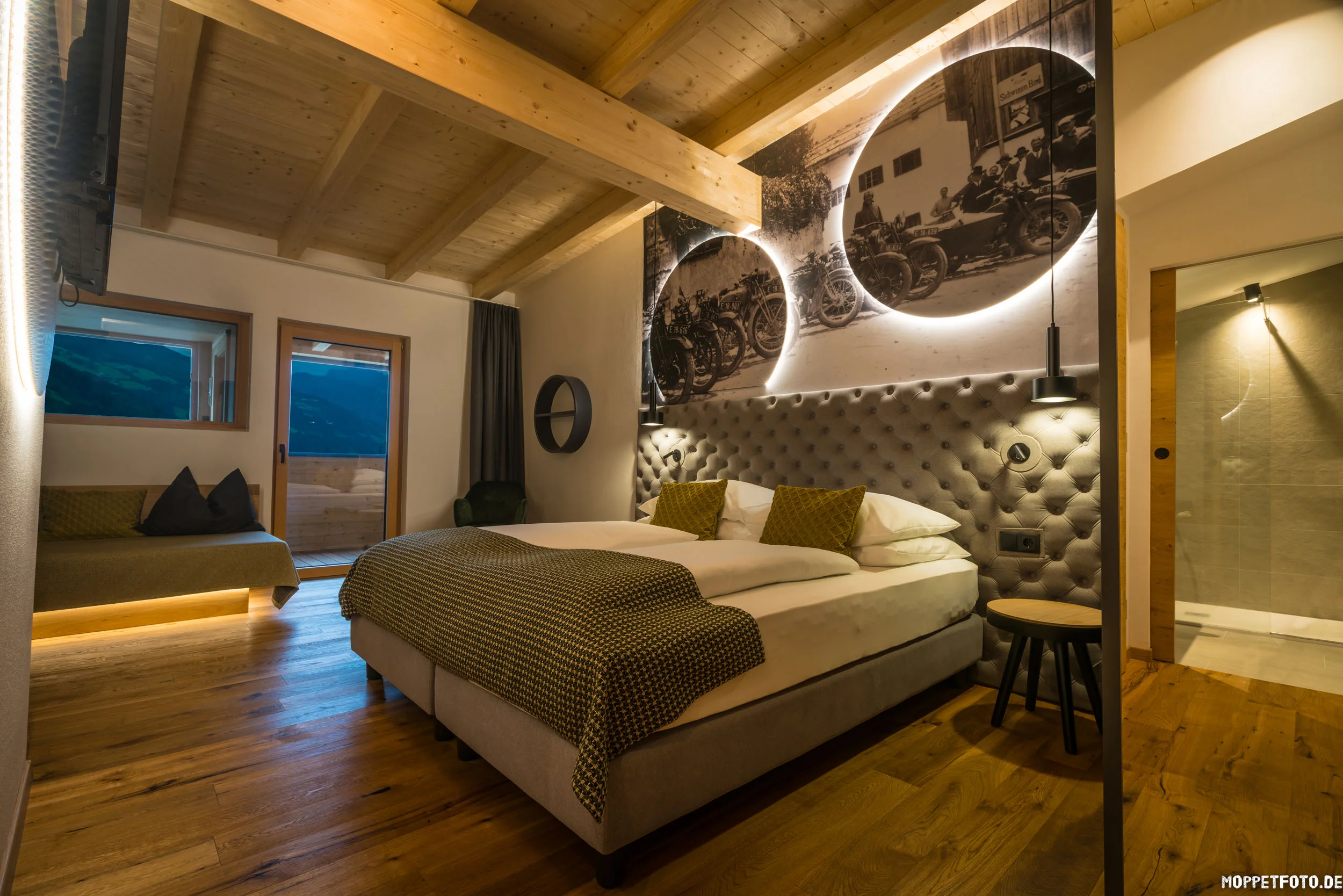 Gemütliches Hotelzimmer mit Holzboden und beleuchtetem Vintage-Motorradbild