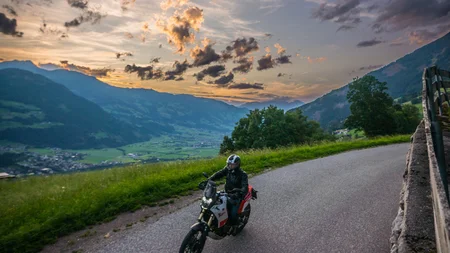 Motorrijder op landweg bij zonsondergang in bergachtig gebied