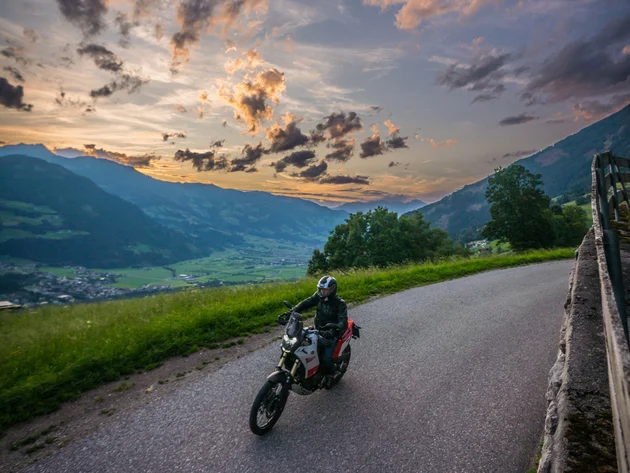 Motorrijder op landweg bij zonsondergang in bergachtig gebied