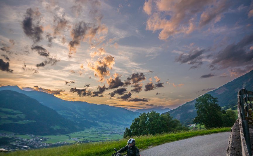 Motorradfahrer auf Landstraße bei Sonnenuntergang in bergiger Landschaft