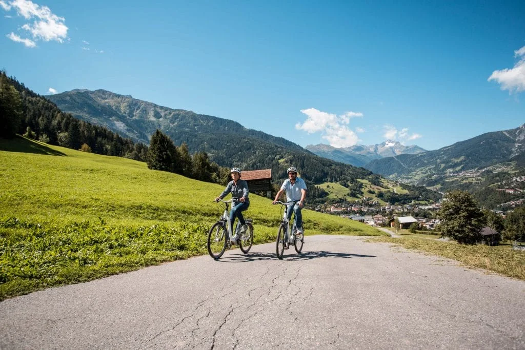 Zwei Personen fahren bei sonnigem Wetter mit Fahrrädern auf einem Bergweg