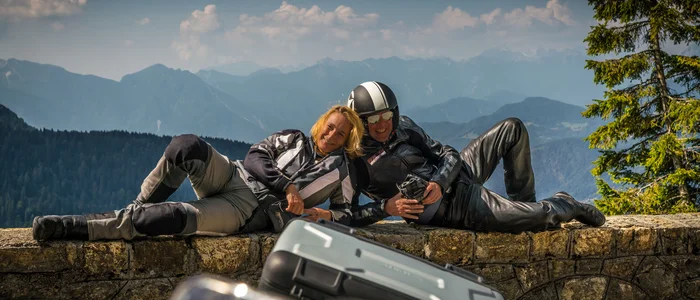 Two motorcyclists relaxing on a wall with mountain scenery