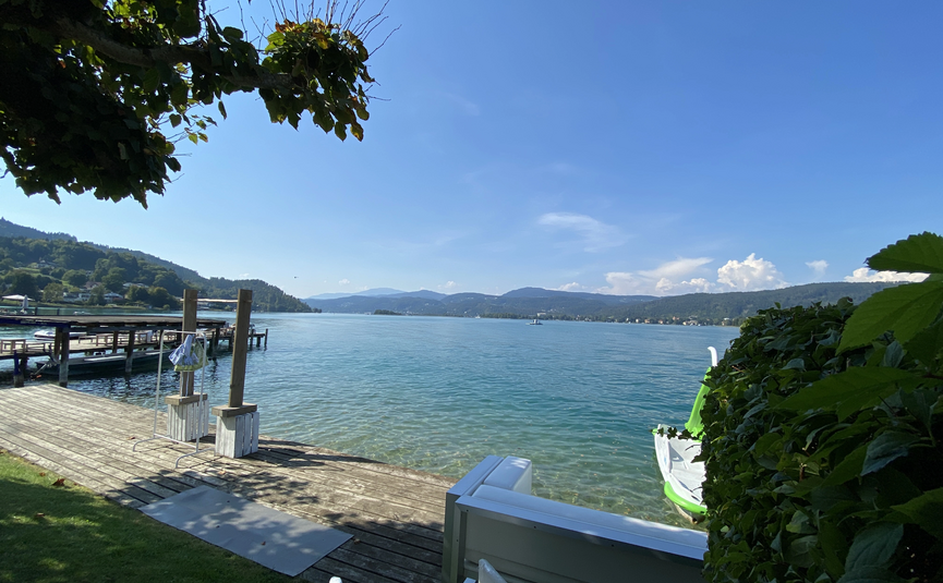 See mit Steg, grünem Ufer und Bergen bei klarem Himmel